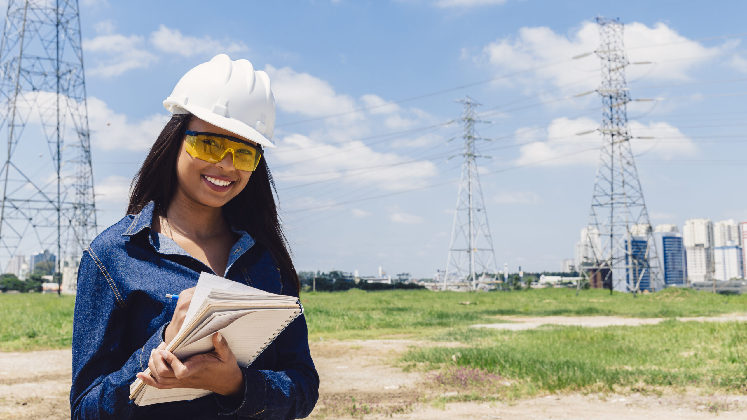 smiling-african-american-lady-safety-helmet-taking-notes-near-high-voltage-line